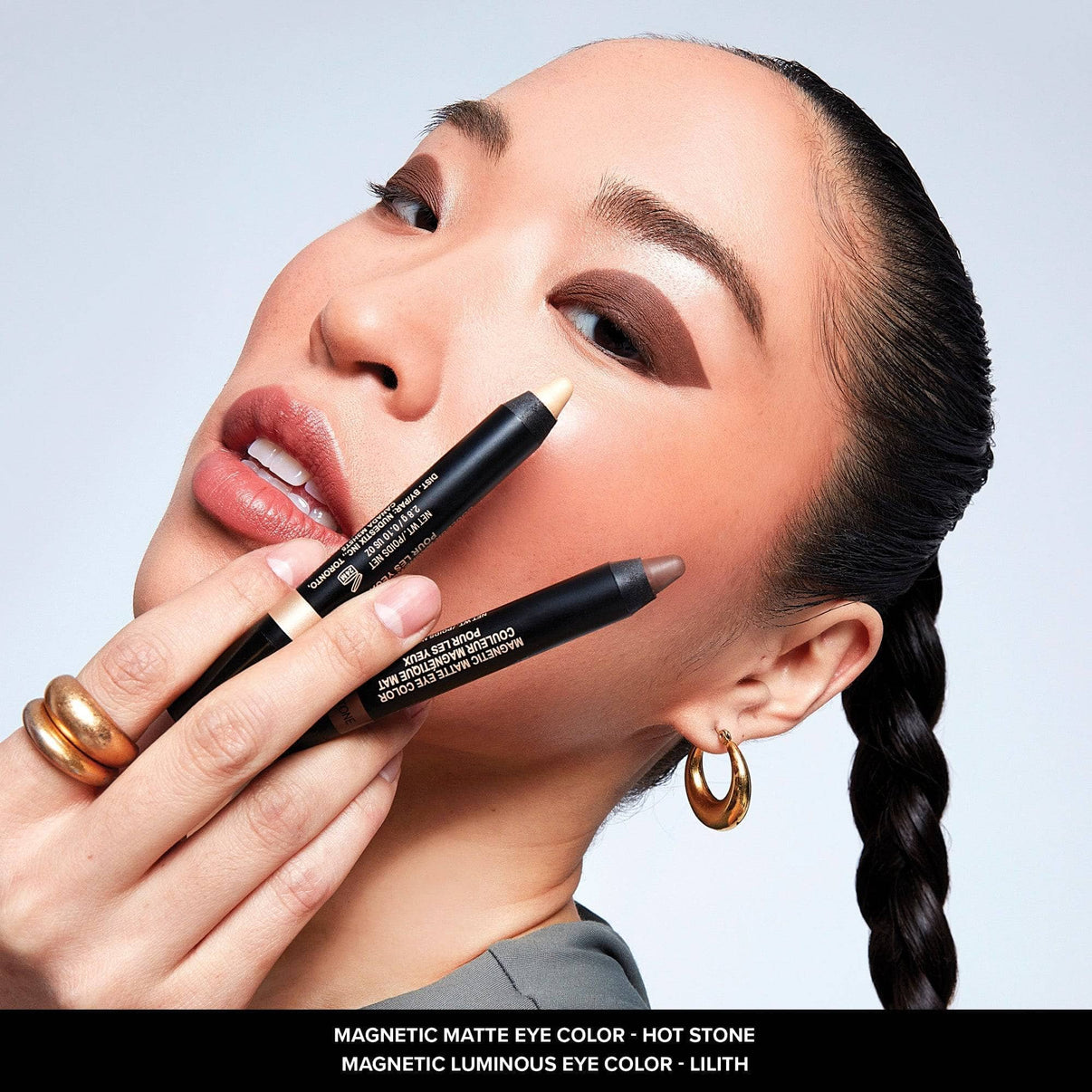 Asian young woman holding magnetic eye color pencils in shades Hot Stone and Lilith