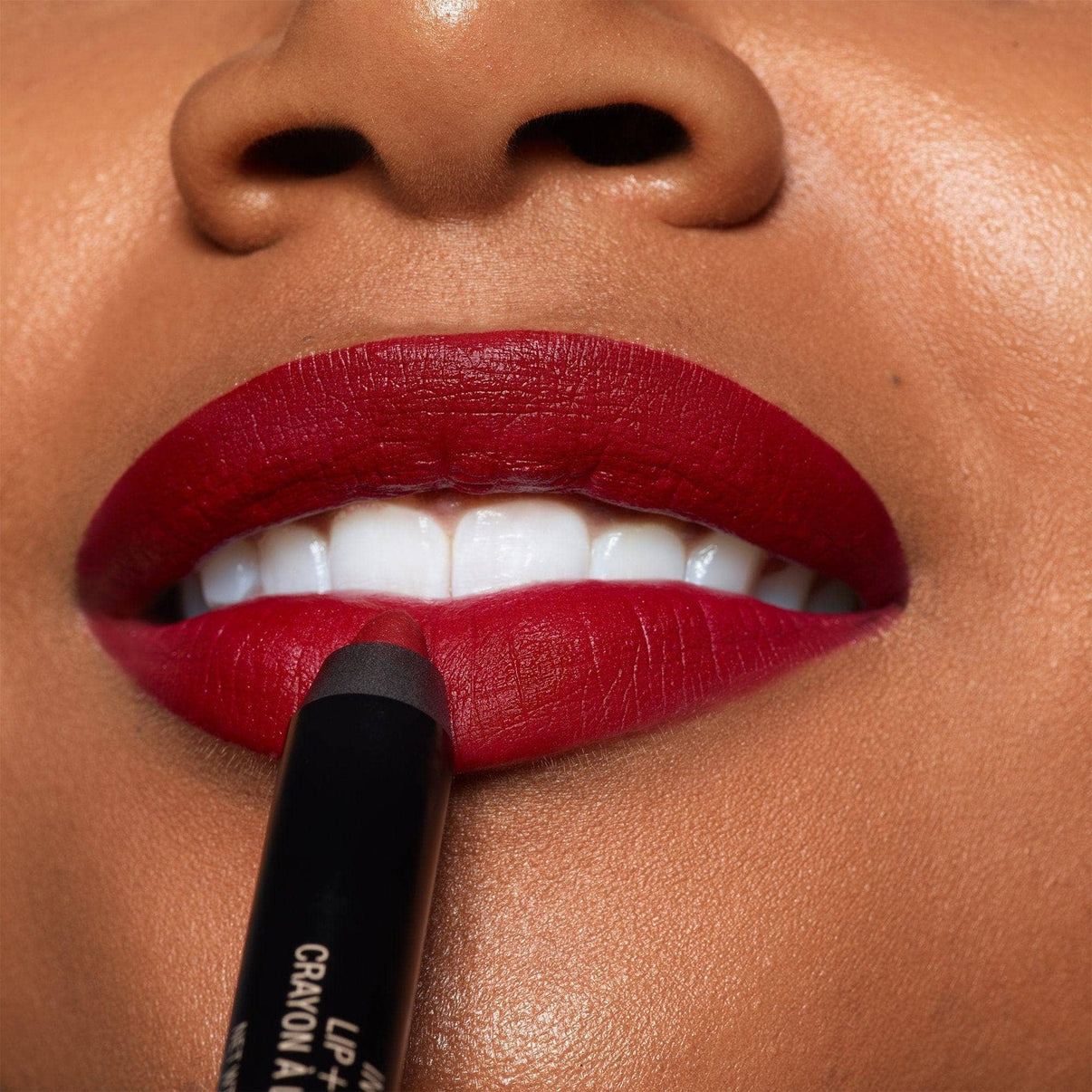 Dark skinned young woman applying  Intense Matte Lip + Cheek pencil in shade raven on her lips